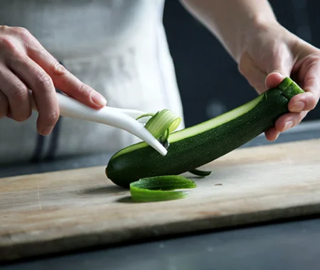 Food professional peeling a zucchini with a peeler on a wooden cutting board