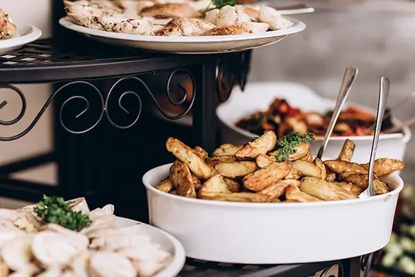 Catered food display with roasted potato wedges, sliced chicken, and mixed dishes on tiered serving stands