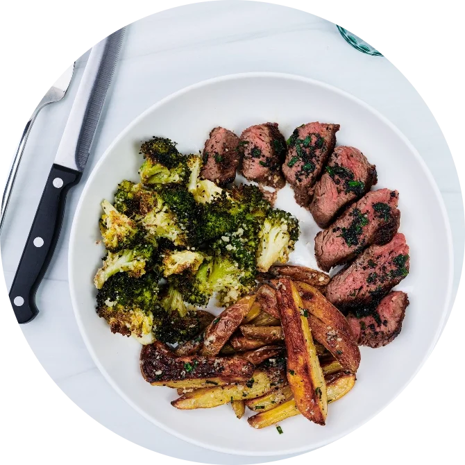 Truffle butter steak with roasted broccoli and fries served on a white plate