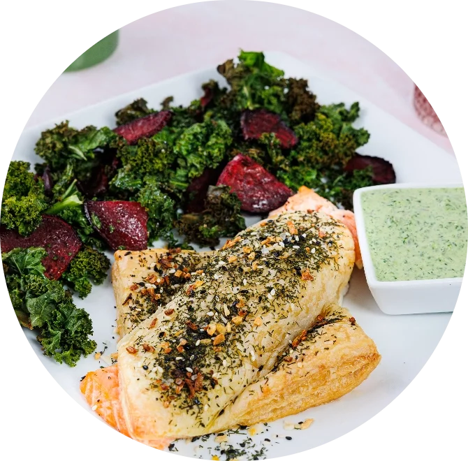 Herb-crusted salmon with roasted kale, beets, and green herb sauce on a white plate