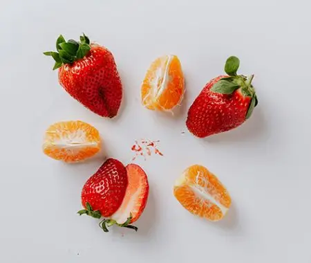 Sliced strawberries and mandarin orange segments arranged on white background