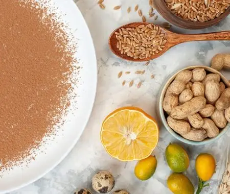 Brown flour on plate with wheat grains, peanuts, citrus, and quail eggs on marble surface