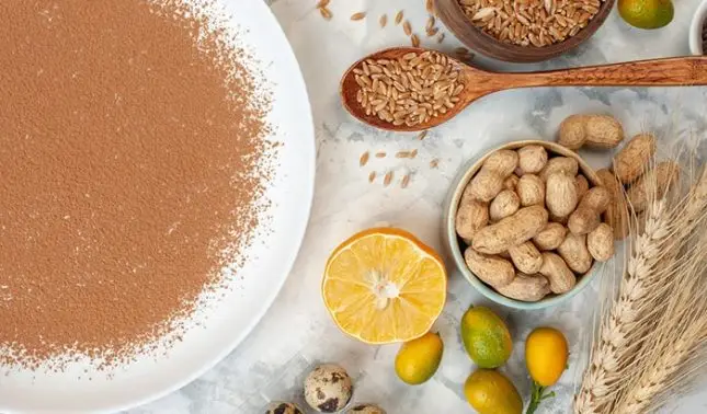Brown flour on plate with wheat grains, peanuts, citrus, and quail eggs on marble surface