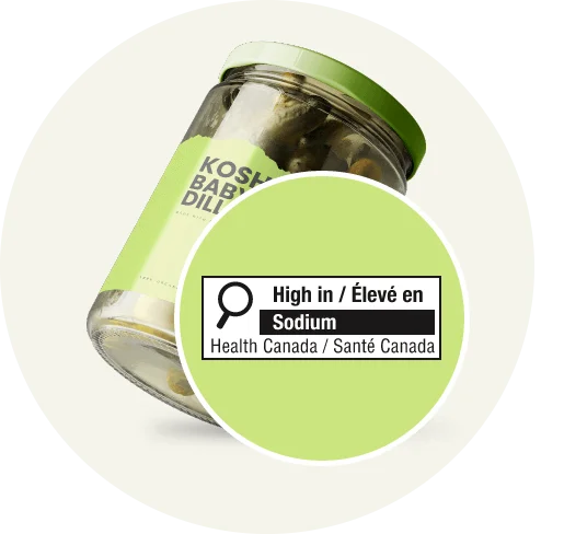 Glass jar of kosher baby dill pickles featuring a Health Canada front-of-pack label warning in a green circle for high sodium content.