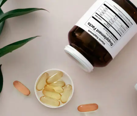 Supplement bottle with Supplement Facts label tipped over with capsules and softgels spilling out