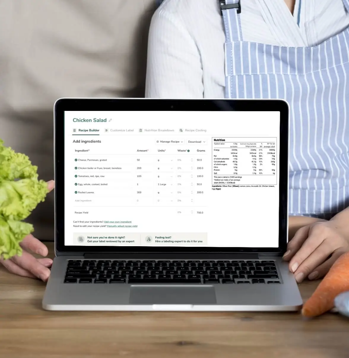 Chef using Food Label Maker on laptop to manage restaurant recipe nutrition data with fresh vegetables nearby