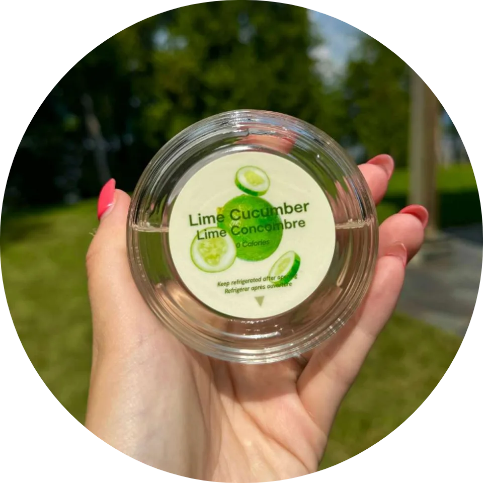 Consumer holding lime cucumber flavored beverage enhancer container outdoors, demonstrating clear product labeling and calorie disclosure.